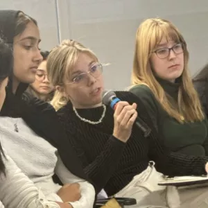 Woman, center, holding microphone and speaking, flanked by three women on either side.