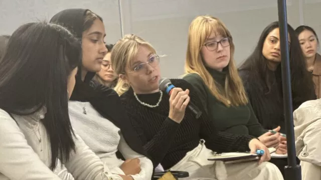 Woman, center, holding microphone and speaking, flanked by three women on either side.